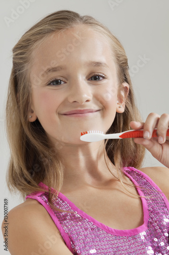 Portrait of young girl holding toothbrush against gray background