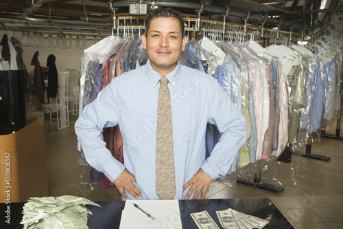 Portrait of confident laundry owner with receipts, notepad and banknotes standing at counter