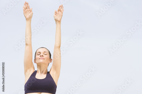 Woman stretches arm up with eyes closed against clear sky