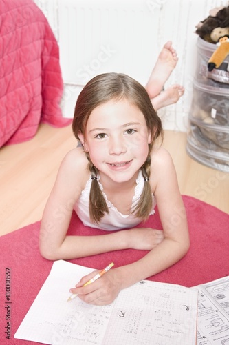Portrait of a young girl lying on floor and doing homework