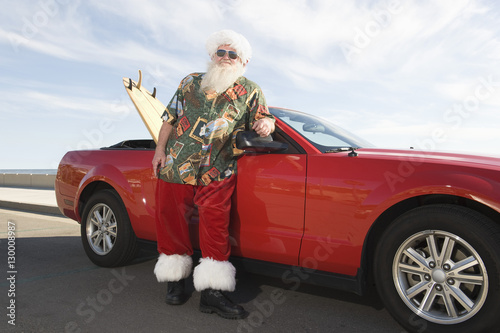 Father Christmas stands by red convertible with surfboard