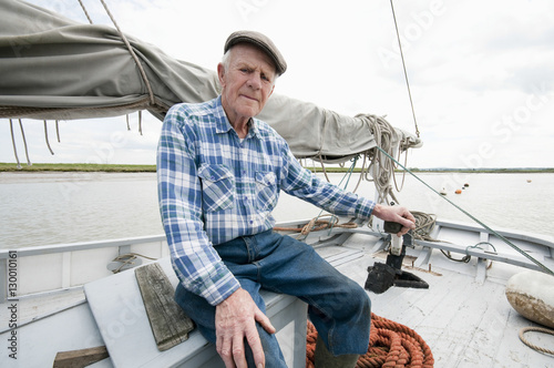 Portrait of a senior fisherman siting on deck of boat with mast and sail
