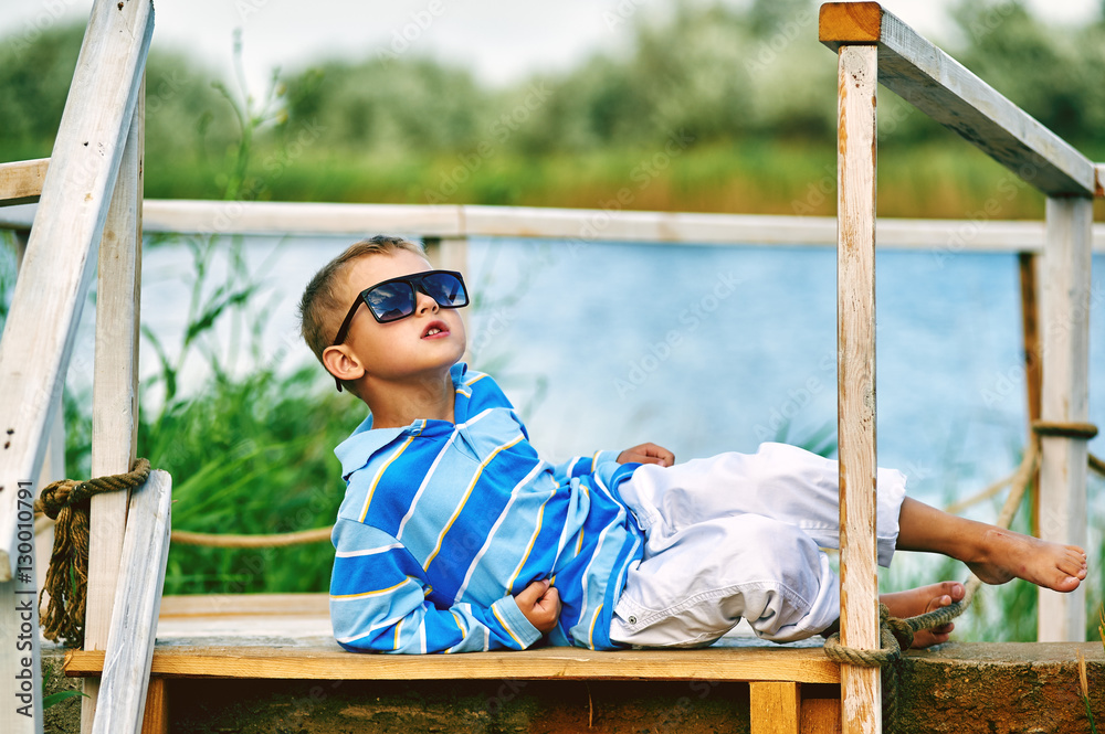 beautiful boy posing on a wooden bridge . Dressed in a nautical style beautiful boy posing on a wooden bridge . Dressed in a nautical style