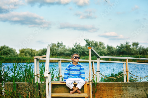 beautiful boy posing on a wooden bridge . Dressed in a nautical style 