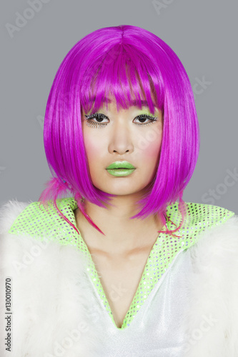 Portrait of young woman wearing pink wig over gray background