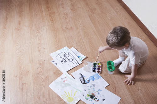 Elevated view of young boy painting with watercolors and paintbrush on laminated floor photo