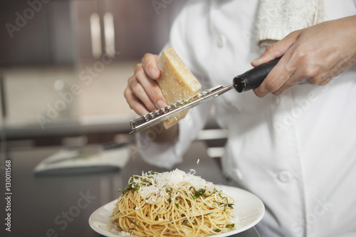 Midsection of female chef grating cheese onto pasta in kitchen photo