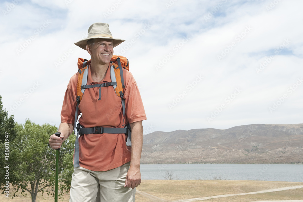 Happy middle age hiker with walking pole and backpack in front of lake
