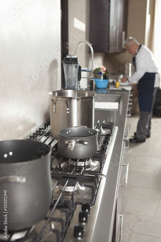 Closeup of utensils on stove with chef working in background at commercial kitchen