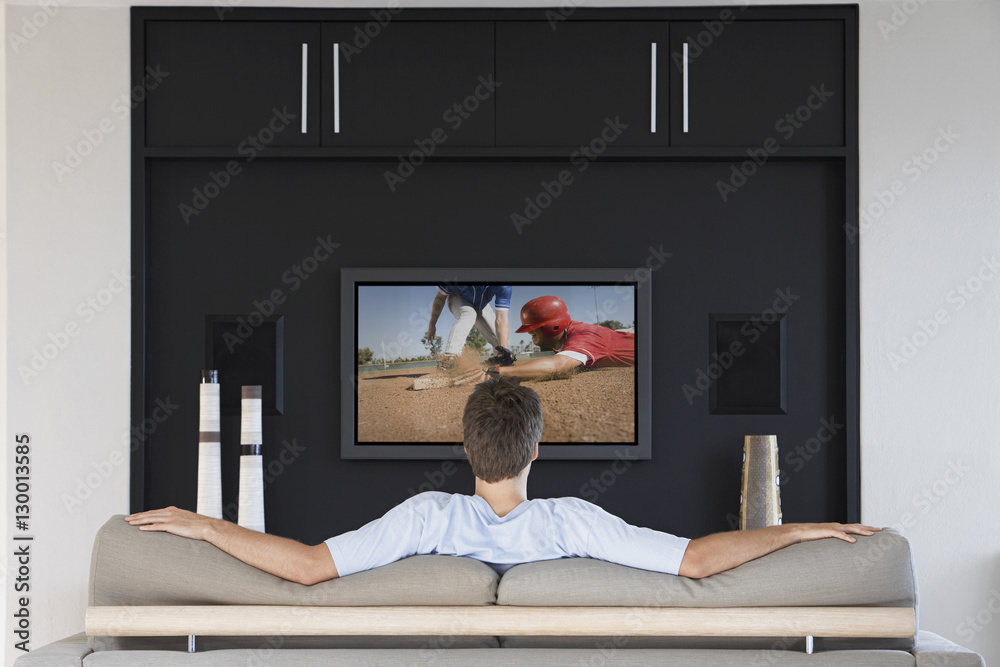 Φωτογραφία Back view of mid-adult man watching baseball game on television in living room