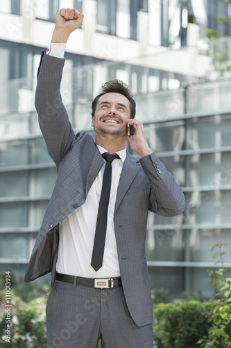 Excited young businessman using cell phone outside office