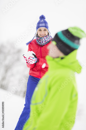 Smiling young woman having snowball fight with male friend