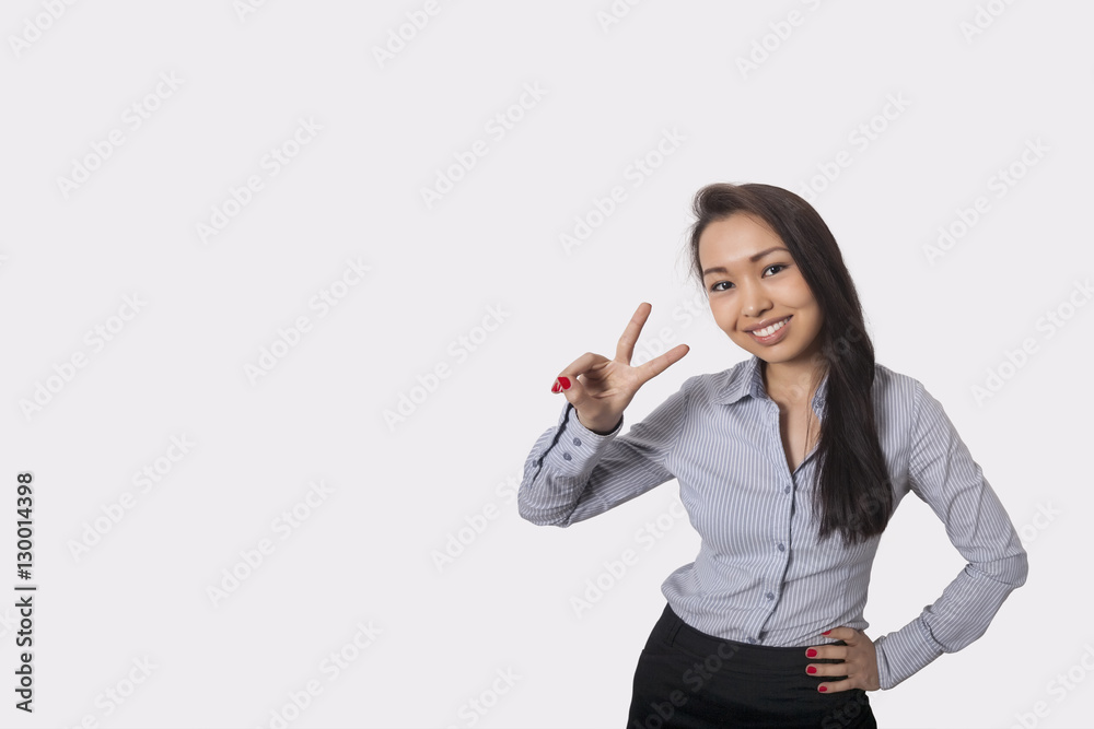 Portrait of happy businesswoman showing victory sign against gray background Portrait of happy businesswoman showing victory sign against gray background
