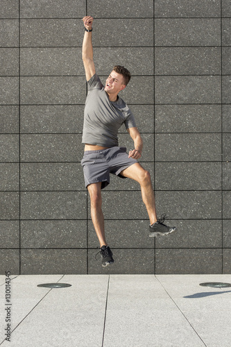 Full length of excited jogger jumping against tiled wall