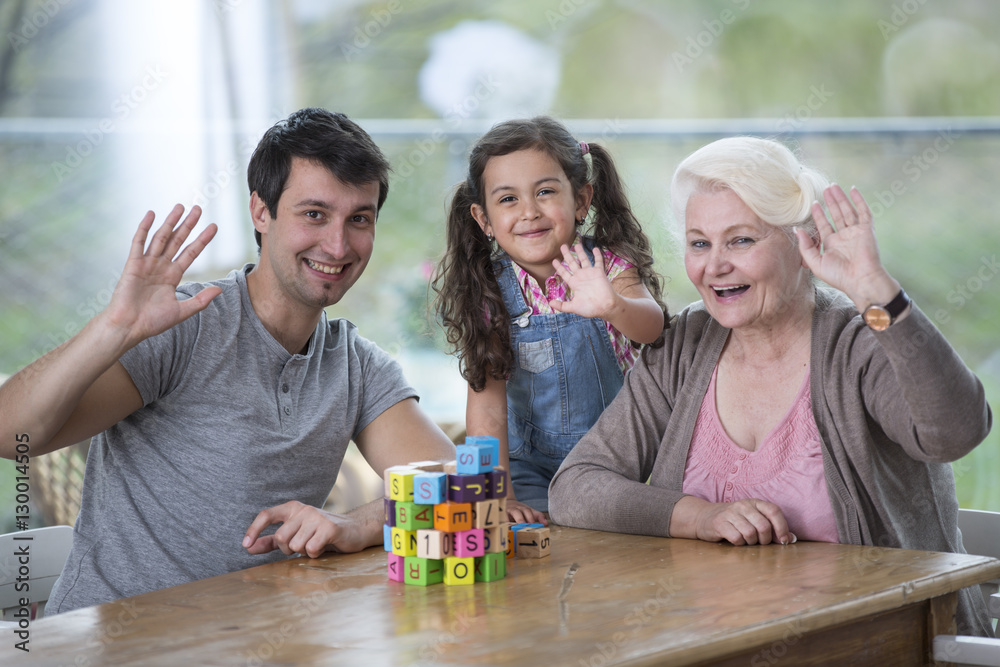 Obraz premium Portrait of senior woman with son and granddaughter waving hands at table
