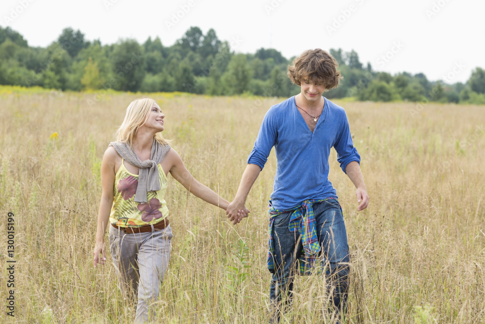 Young couple holding hands while walking through field Young couple holding hands while walking through field