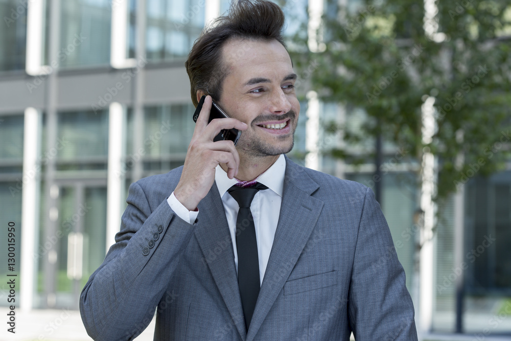 Happy businessman conversing on cell phone outside office Happy businessman conversing on cell phone outside office