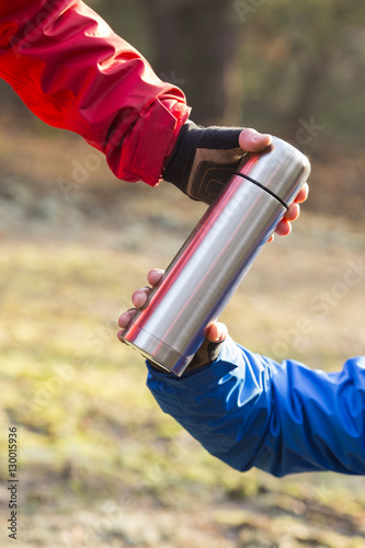 Cropped image of hikers holding insulated coffee container in forest