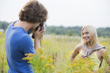 Young man photographing girlfriend in field