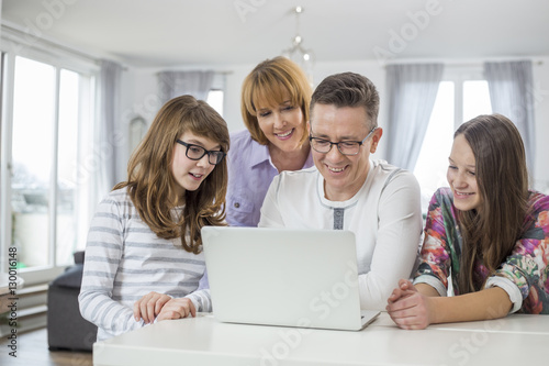 Family of four using laptop together at table in home