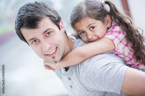 Side view portrait of smiling man piggybacking little daughter at home
