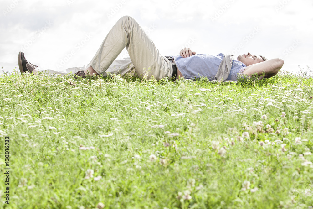 Full length of young man lying on grass against sky Full length of young man lying on grass against sky