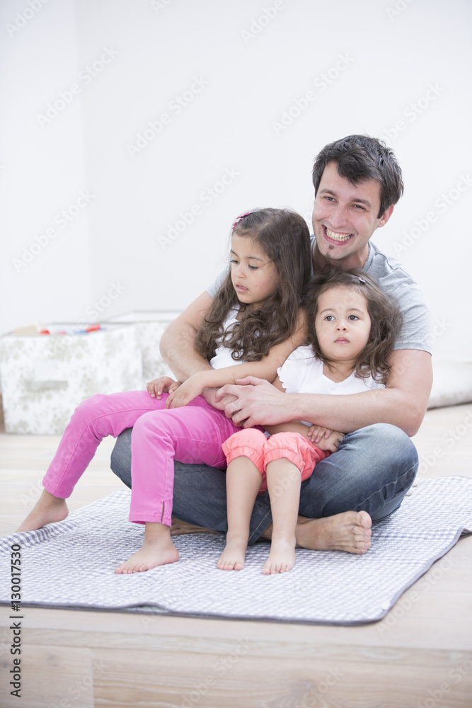 Smiling young man with daughters sitting in his lap at home Smiling young man with daughters sitting in his lap at home