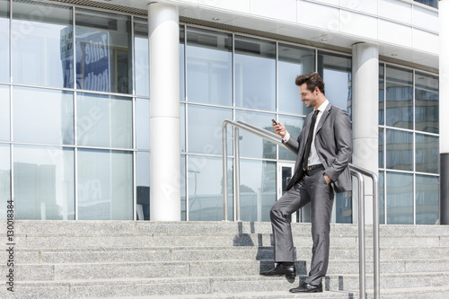 Full length of businessman text messaging through cell phone while standing on steps outside office