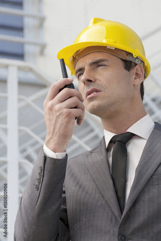 Young male architect talking on walkie-talkie against building