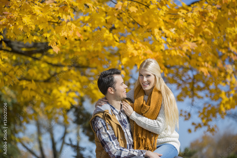 Portrait of happy woman sitting on man's lap in park during autumn