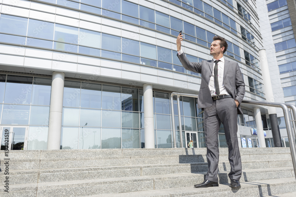 Full length of businessman taking self portrait on steps outside office Full length of businessman taking self portrait on steps outside office