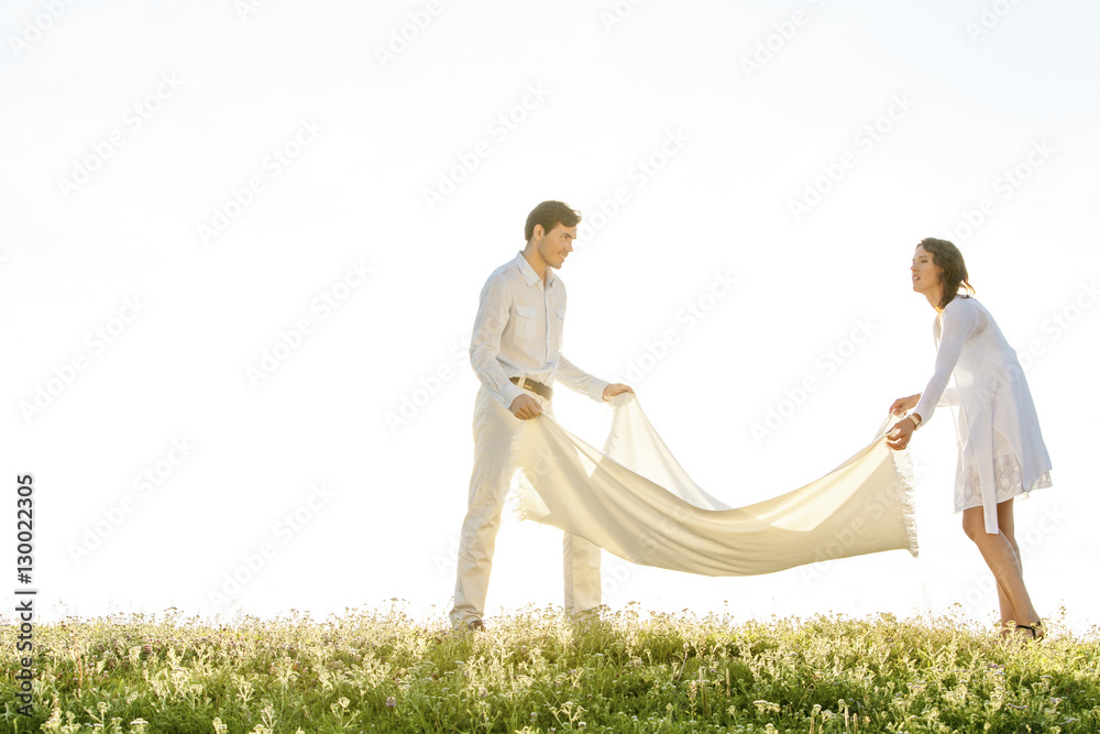 Young couple spreading picnic blanket on grass during sunny day Young couple spreading picnic blanket on grass during sunny day