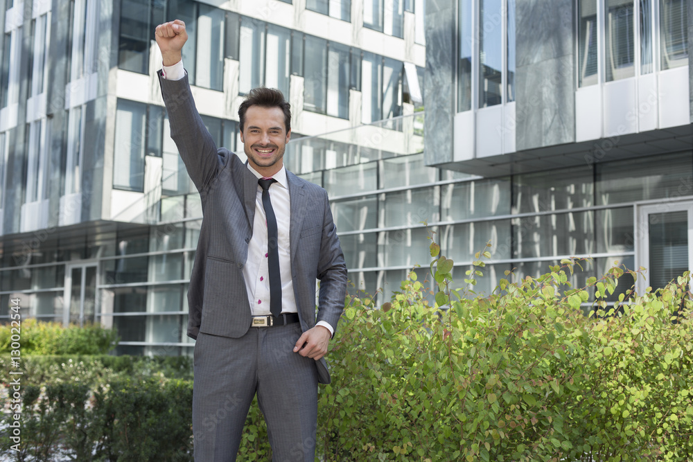 Portrait of successful businessman with arm raised standing outside office building Portrait of successful businessman with arm raised standing outside office building