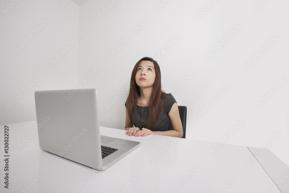 Thoughtful young businesswoman looking up with laptop at office desk Thoughtful young businesswoman looking up with laptop at office desk