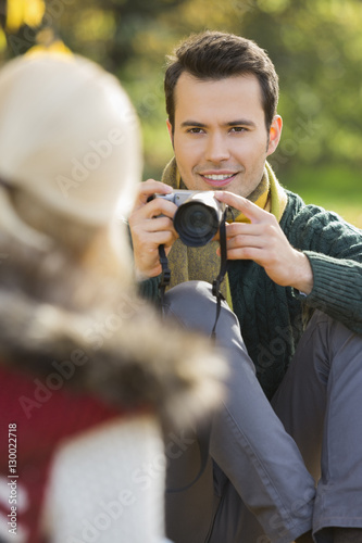 Smiling young man photographing woman in park