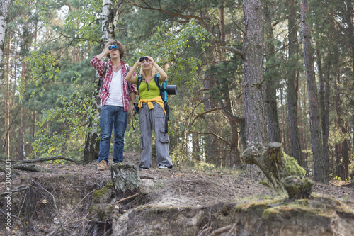 Hiking couple using binoculars in forest