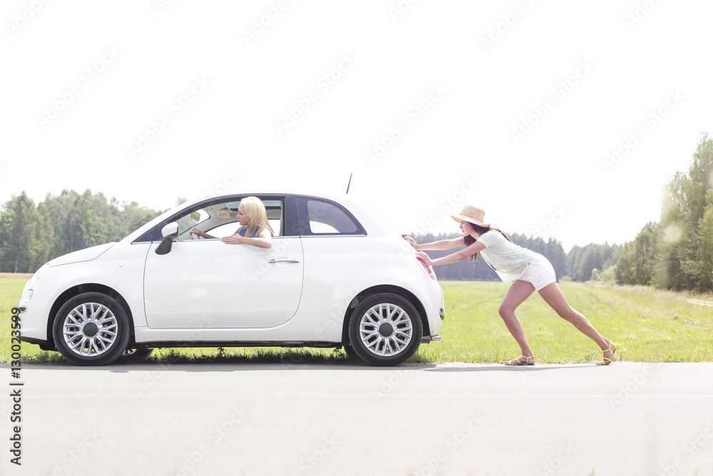 Woman pushing broken down car on country road