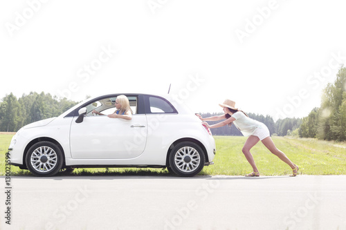 Woman pushing broken down car on country road © moodboard