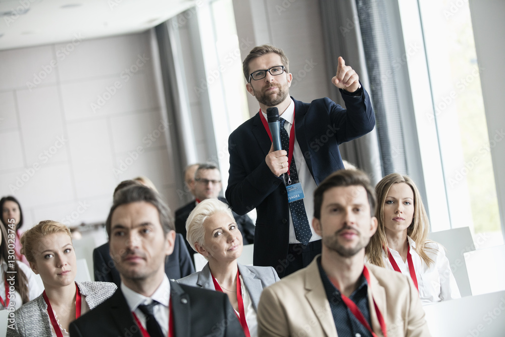 Businessman gesturing while asking question during seminar in convention center Businessman gesturing while asking question during seminar in convention center
