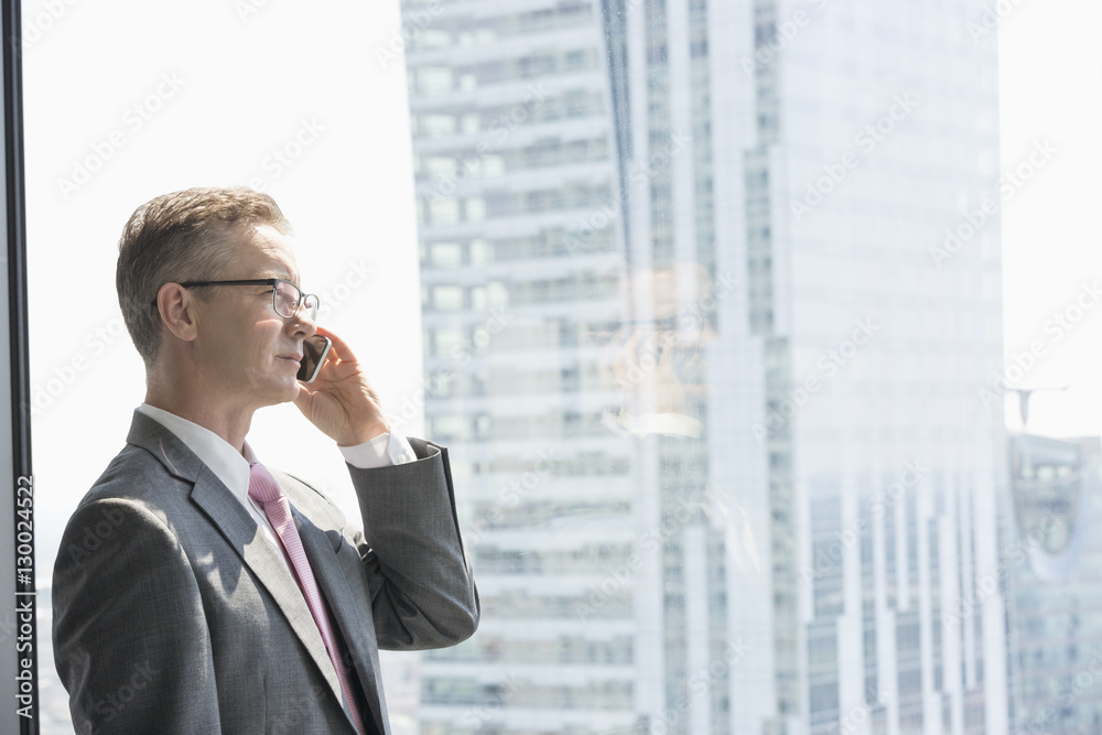 Mature businessman talking on cell phone by window Mature businessman talking on cell phone by window