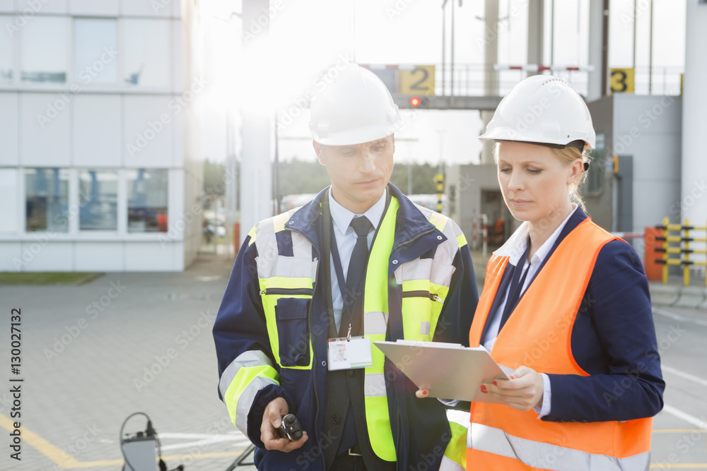 Male and female workers discussing over clipboard in shipping yard Male and female workers discussing over clipboard in shipping yard