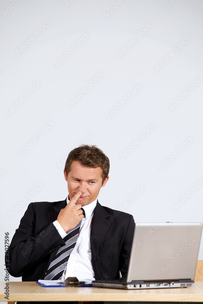 Businessman picking nose, looking at laptop in office Businessman picking nose, looking at laptop in office