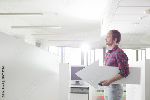 Side view of businessman holding arrow sign in creative office