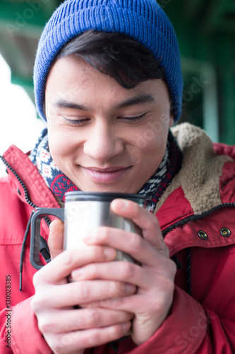 Smiling man looking at coffee in insulated drink container during winter