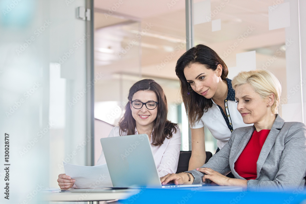 Team of businesswomen using laptop at table in office Team of businesswomen using laptop at table in office
