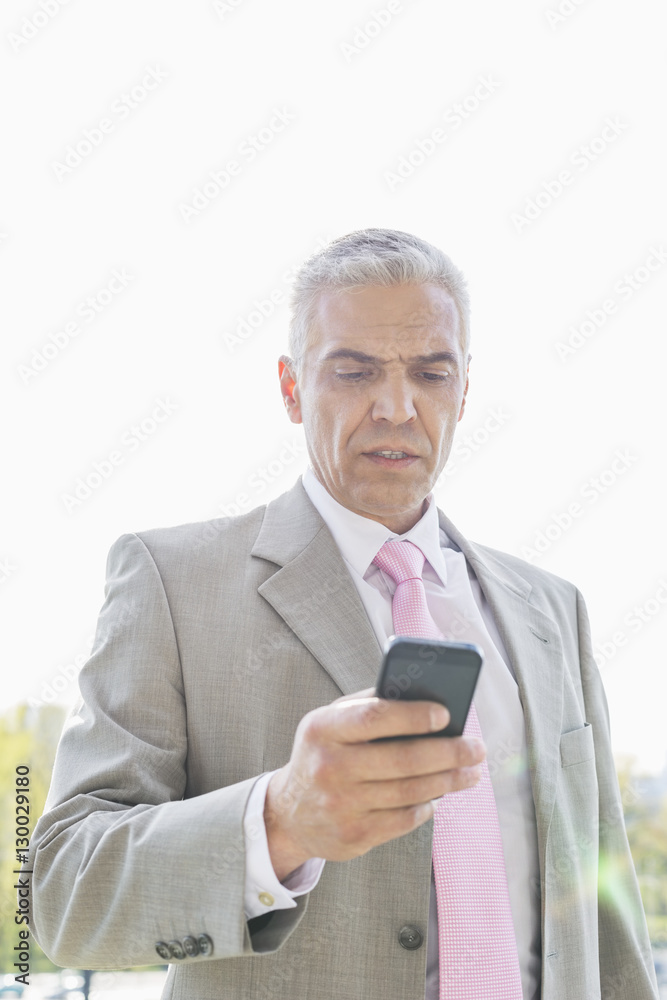 Businessman reading text message on cell phone against sky Businessman reading text message on cell phone against sky