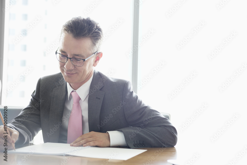 Mature businessman writing on book at table in office