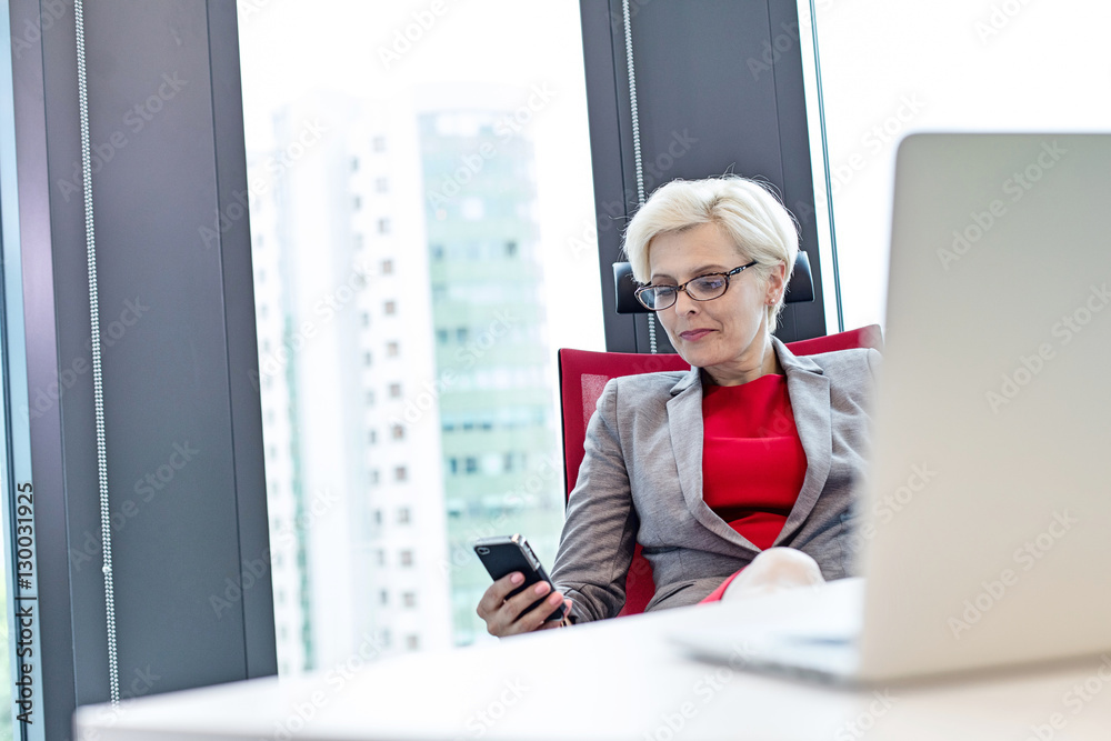 Mature businesswoman using mobile phone at desk in office Mature businesswoman using mobile phone at desk in office
