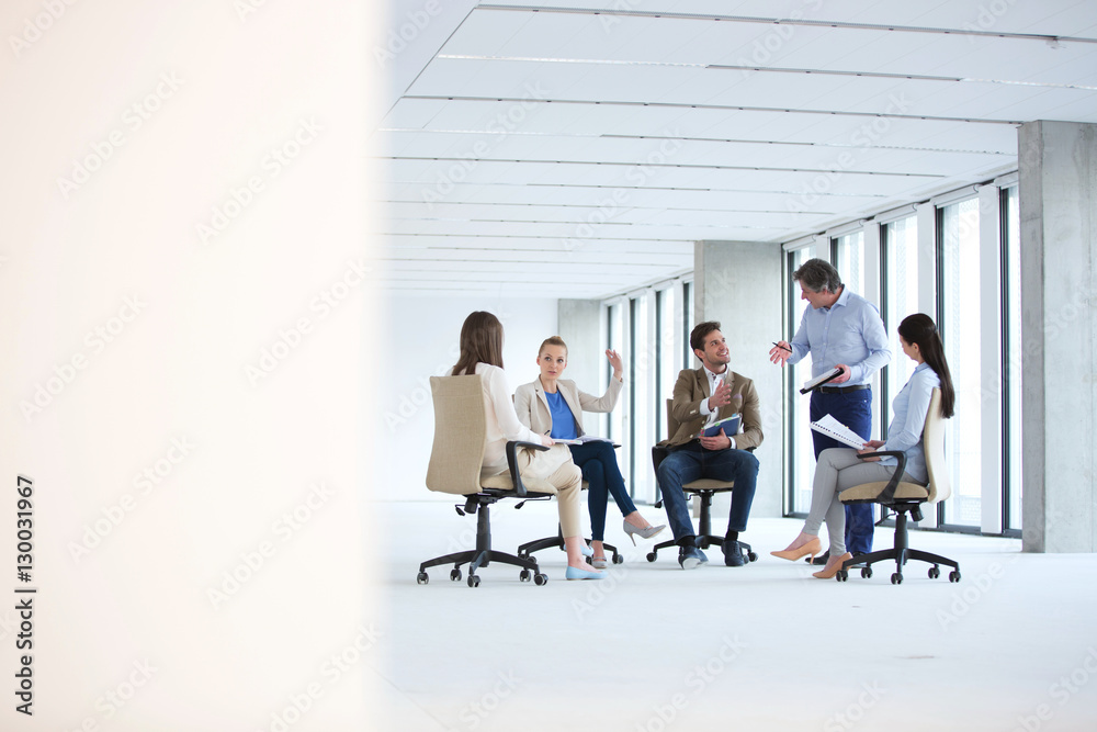 Fototapeta premium Mature businessman discussing with team sitting on chair in new office