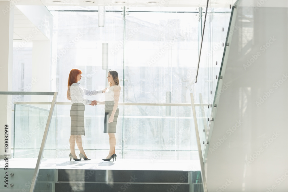 Full-length of businesswomen shaking hands in office Full-length of businesswomen shaking hands in office